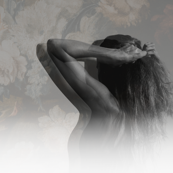 A person with long hair bent over, set against a blurred floral background.