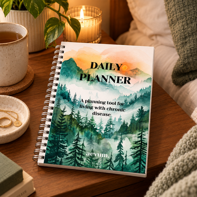 A Daily Planner titled A planning tool for living with chronic disease by Aevum rests on a wooden surface surrounded by plants and candles.