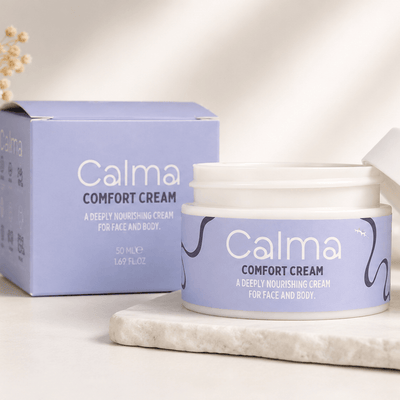 A jar of Calma Comfort Cream and its matching lavender box, styled on a light marble slab against a warm, sunlit neutral background.