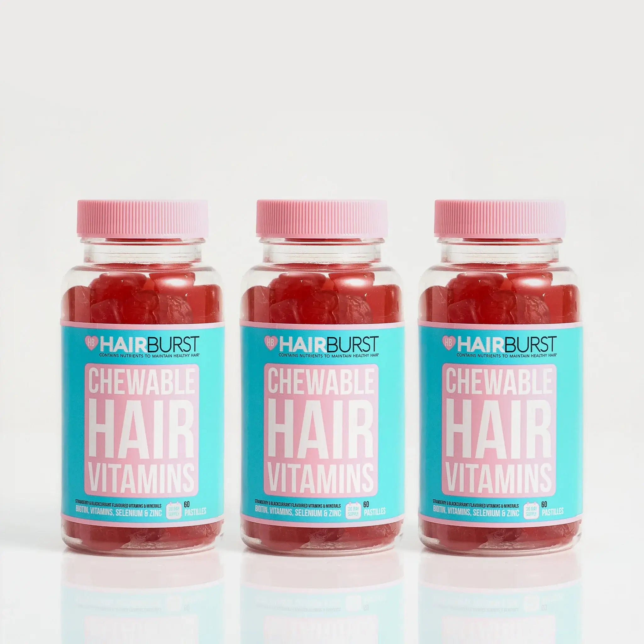 Three bottles of HAIRBURST Chewable Hair Vitamins lined up on a reflective white surface against a light gray background.