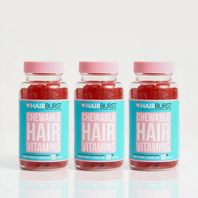 Three bottles of HAIRBURST Chewable Hair Vitamins lined up on a reflective white surface against a light gray background.