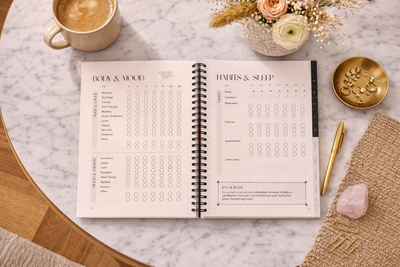 Open planner on a marble surface with coffee, flowers, and a pen.