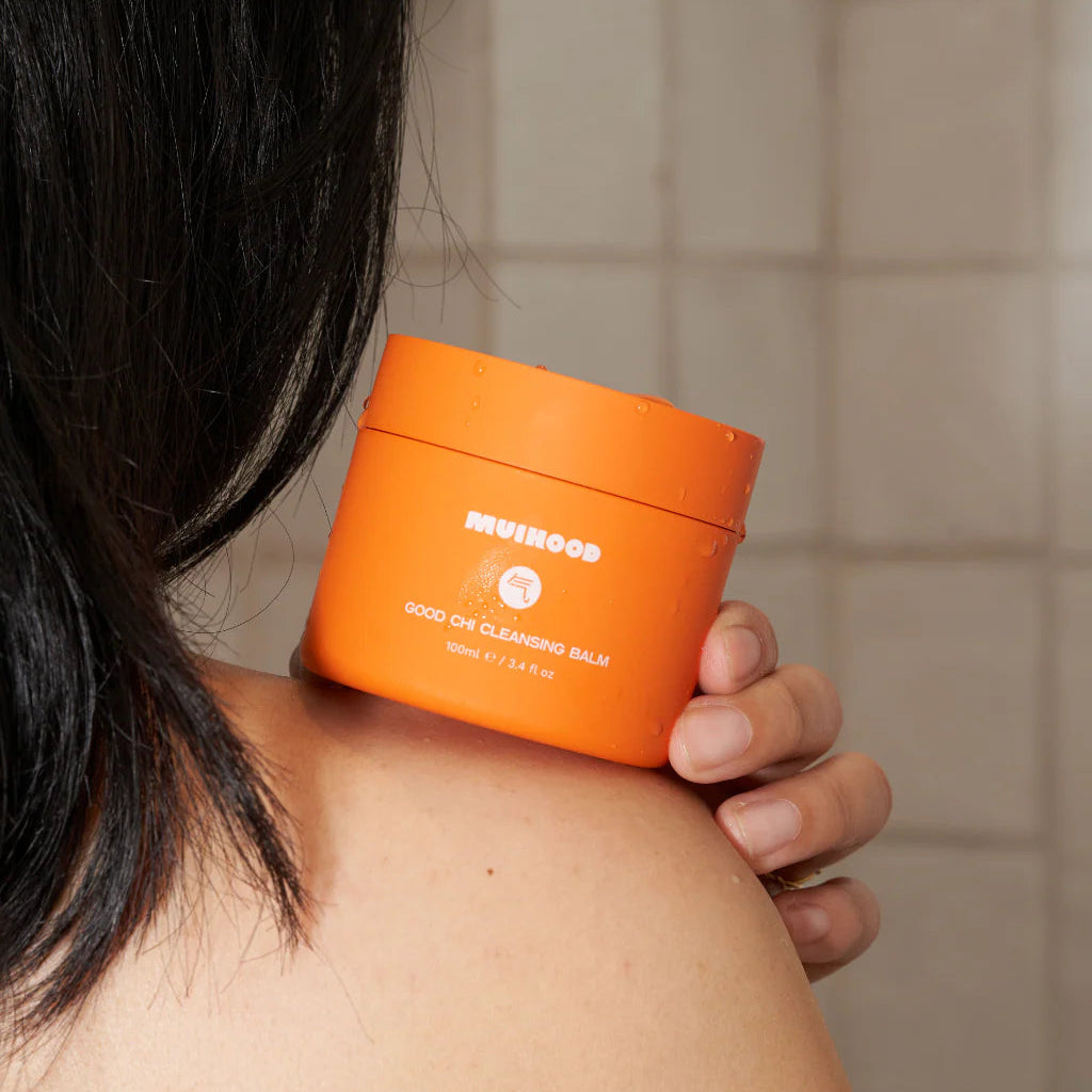 Person holding an orange container labeled 'Muihood' against a tiled wall background