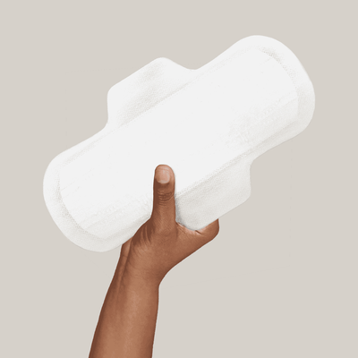 A brown human hand holding a white organic sanitary pad.