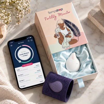 A smartphone displaying fertility cycle data next to an open box containing a Tempdrop Fertility Monitor and a purple pouch.