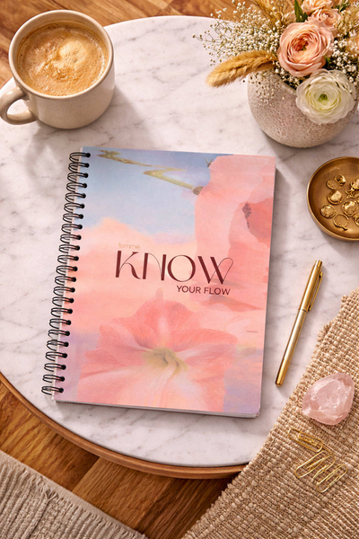 Notebook titled 'KNOW YOUR FLOW' with a cup of coffee, pen, and flowers on a marble surface.