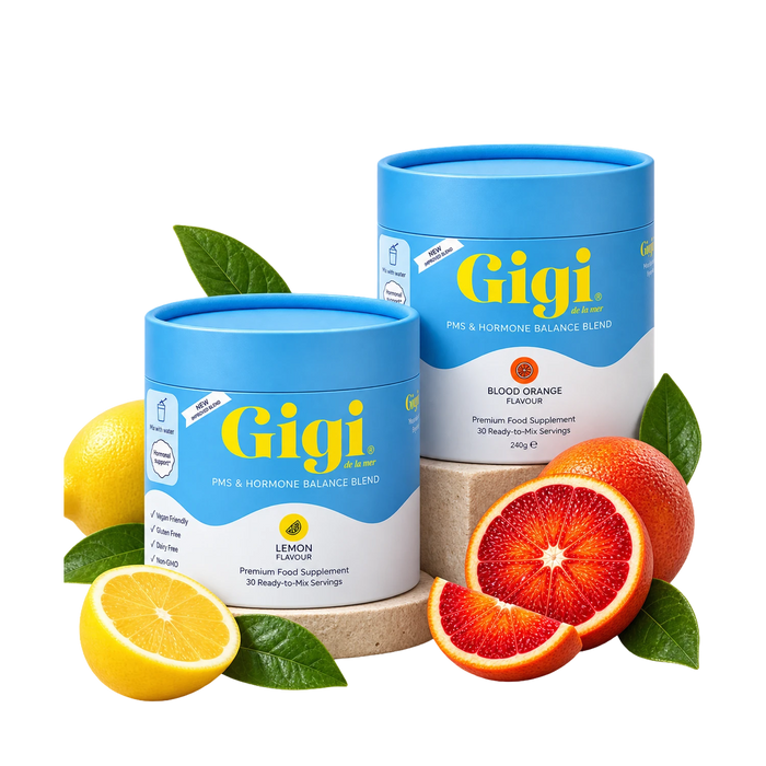 Two Gigi PMS & Hormone Balance Blend containers, lemon and blood orange, styled with fresh fruit on a white background.